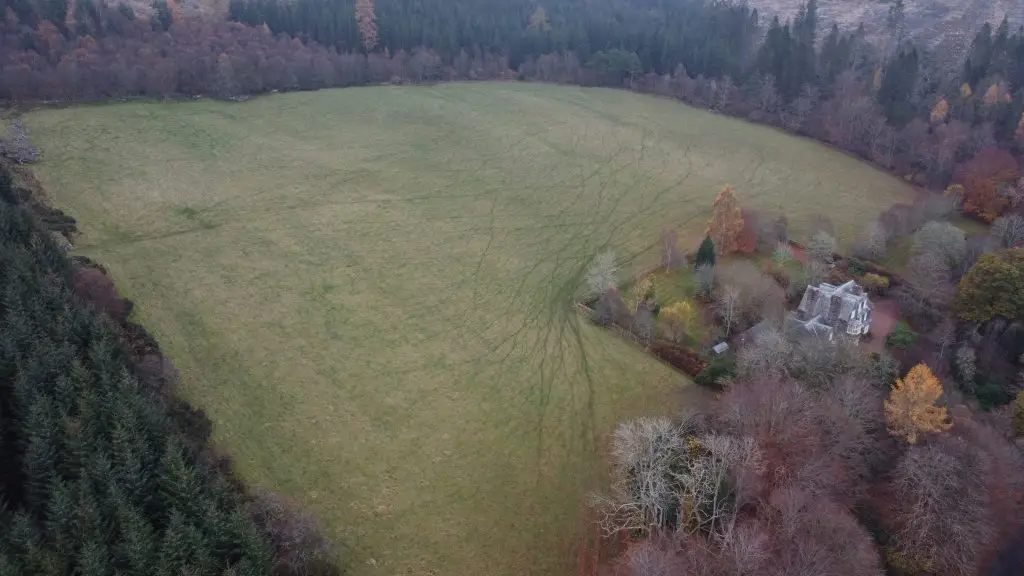 Arial Shot of a large square shaped field surrounded by forest with a house in the bottom right corner
